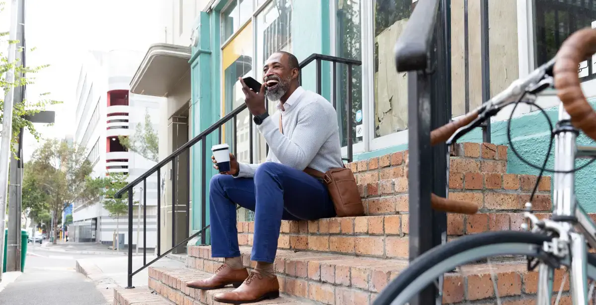 Man sitting on a stoop speaking into the bottom of his smarthone that is held flat in front of him.