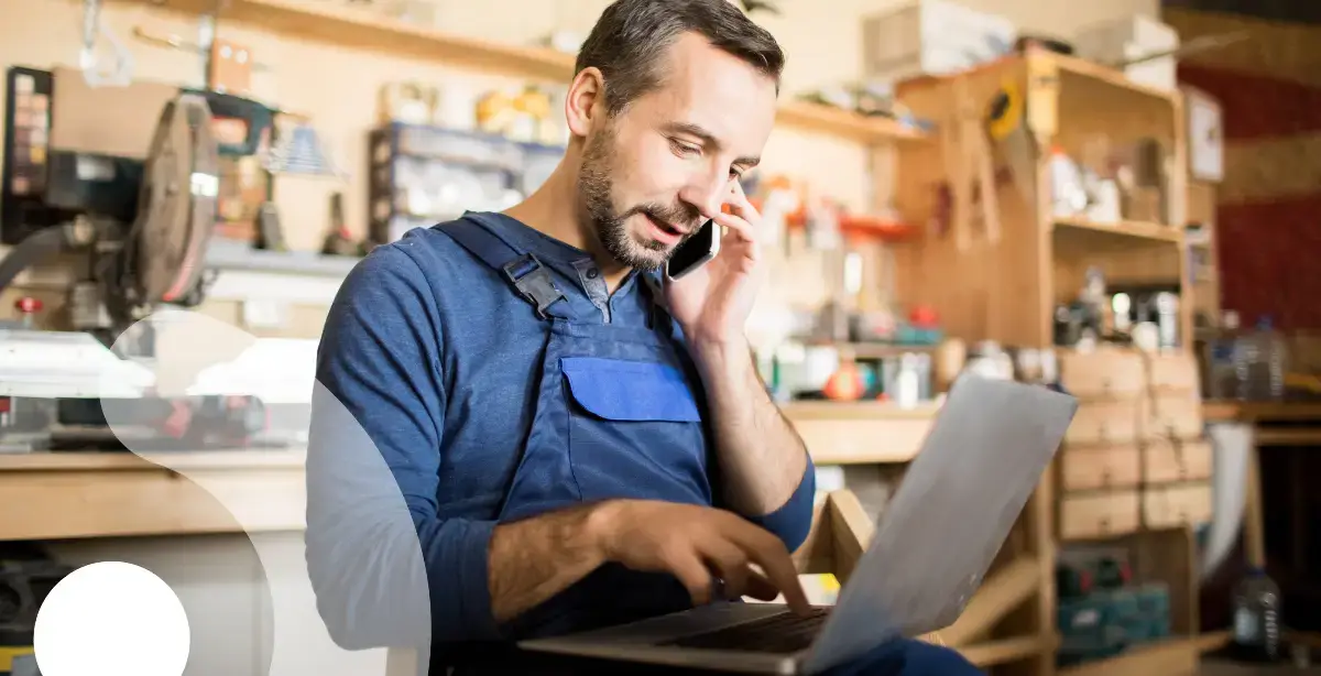 Person in overalls talking on the phone in a work shop environment.