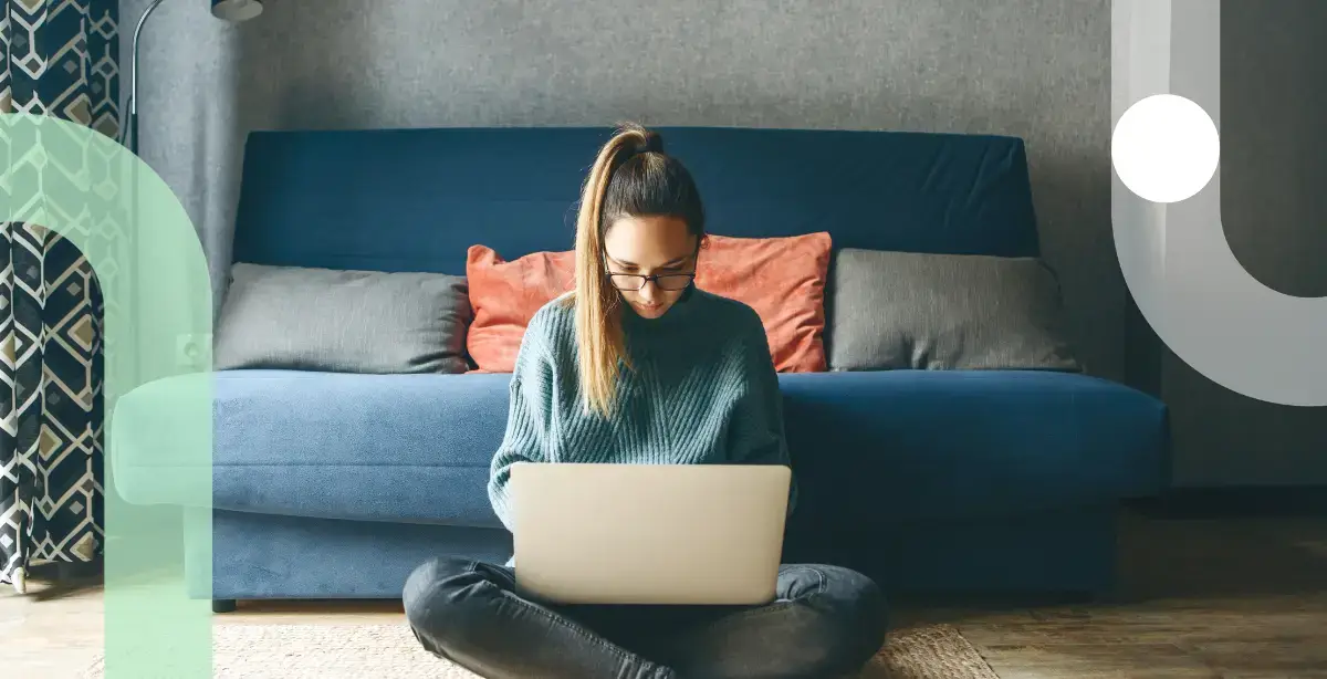 Young woman sitting on a rug by a the sofa at home typing on a laptop.