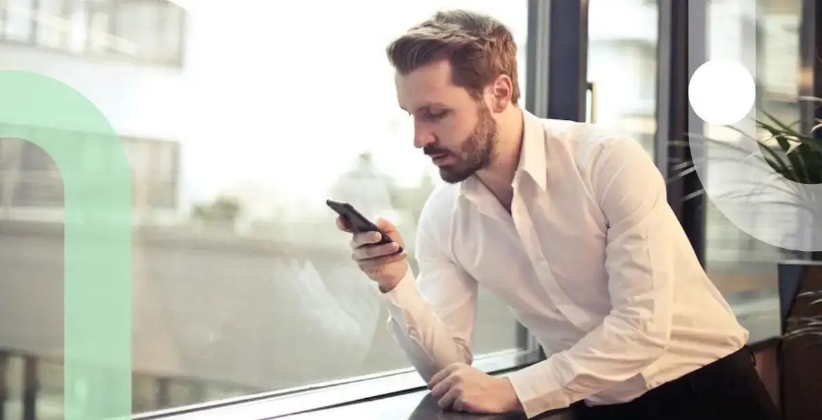 Man by window in office setting looking at his phone.